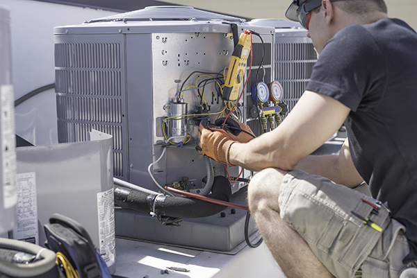 Manasquan HVAC repair technicain shown working on a heating and cooling unit wearing safety gloves and goggles and using yellow tool with red and black wires