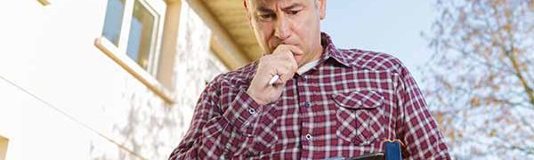 Ortley Beach real estate Ortley Beach real estate home inspector wearing red plaid shirt, wearing white hard hat, and looking at a clipboard he is holding in his left hand